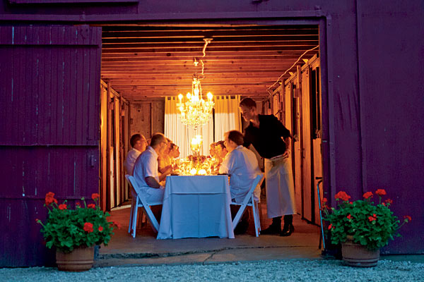 From the outside, the barn glowed like a lantern. Inside, guests enjoyed dinner amid romantic shadows created by candles on the table and chandeliers glittering overhead.