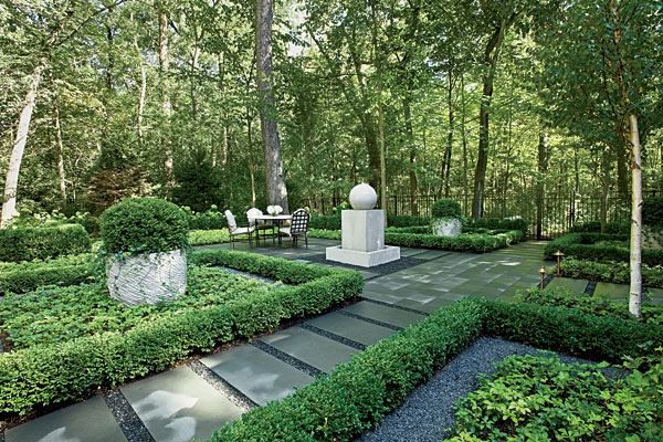 A formal garden with bluestone paths, planters, and fountain, surrounded by trees