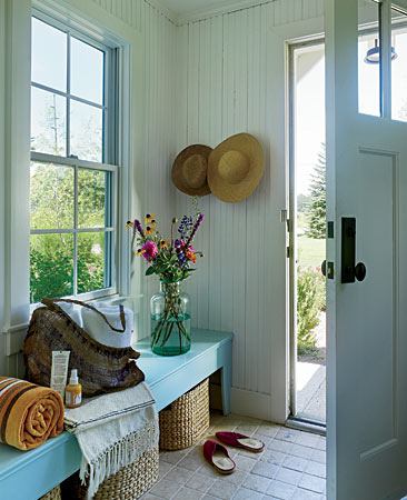 In a cottage in Three Oaks, Michigan, interior designer Julia Edelmann took wainscoting all the way up to the ceiling and put baskets under a rustic turquoise bench to make the space homey and casual.