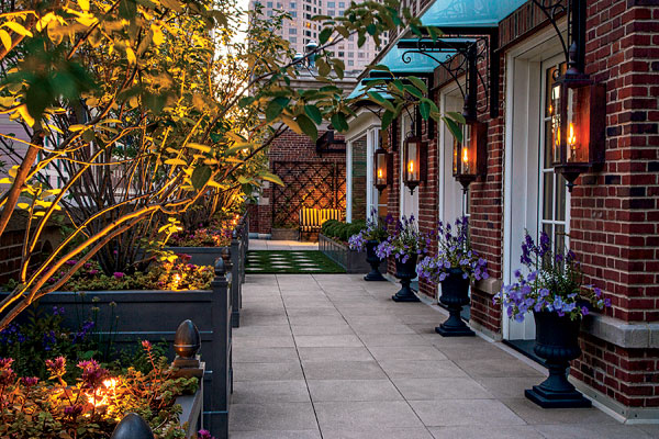 Seasonal plantings that spill out of urns mark the three doorways to the residence. In the background, a patch of synthetic grass offers a convenient place for the owners to exercise their dog.