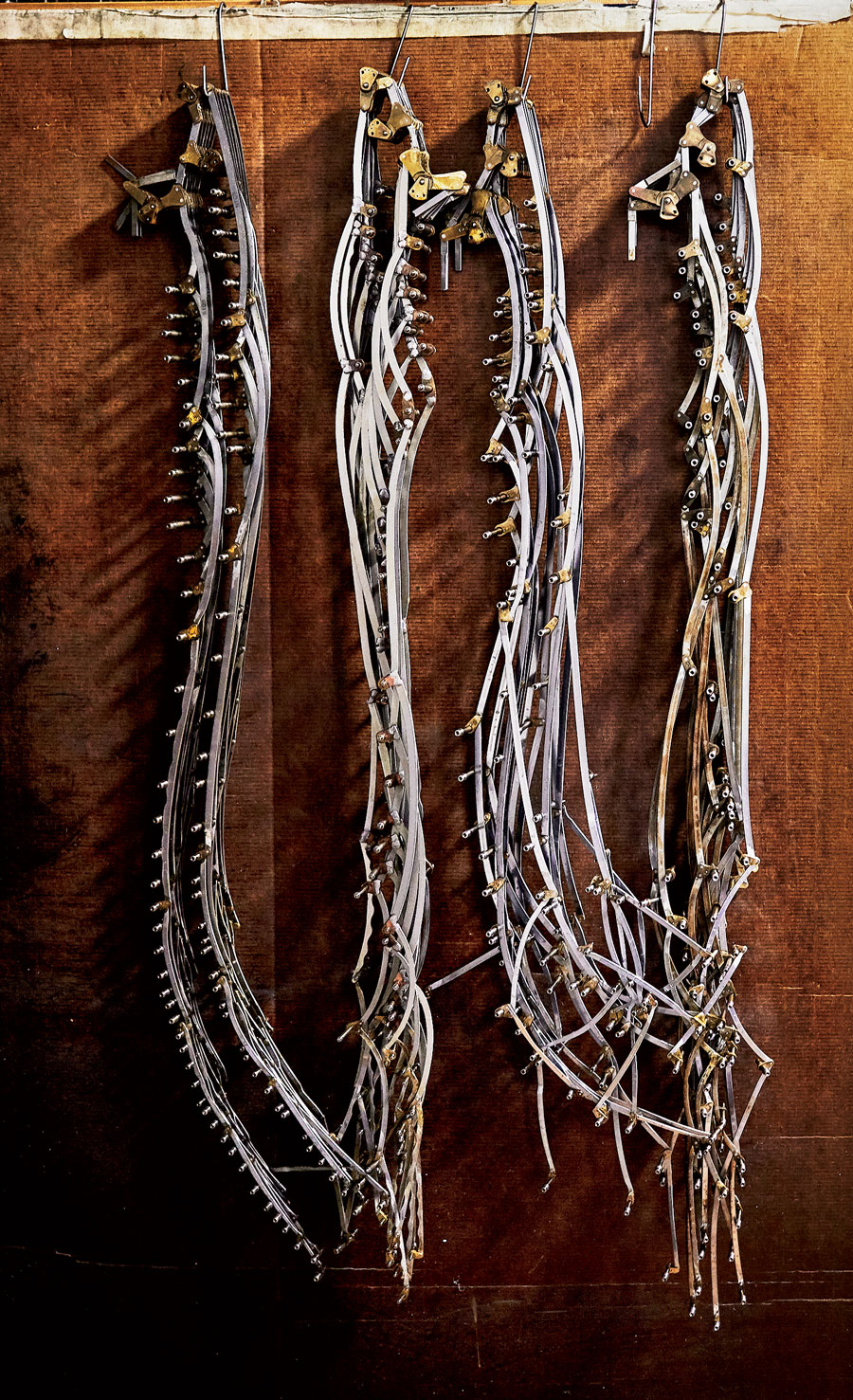 Linkages, the delicate bones that make the mechanism work, dangle from hooks on the wall.