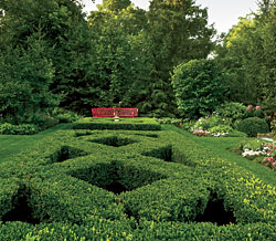 The formal English garden just behind the minimalist Japanese one feels almost like a different world. Anchored by a red bench against a majestic backdrop of Norway spruce, this formal parterre area is planted with lavender, wave petunia, cosmos, verbena, and dianthus.