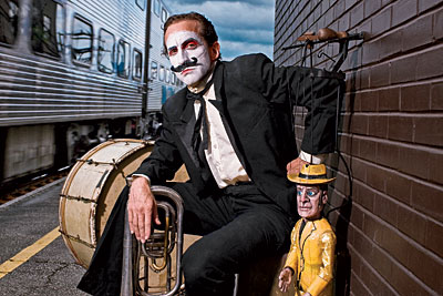 Blair Thomas near train tracks with his marionette and musical instruments