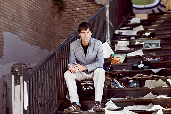 Mason Bates, composer-in-residence with the Chicago Symphony Orchestra, sitting on a staircase littered with music related items