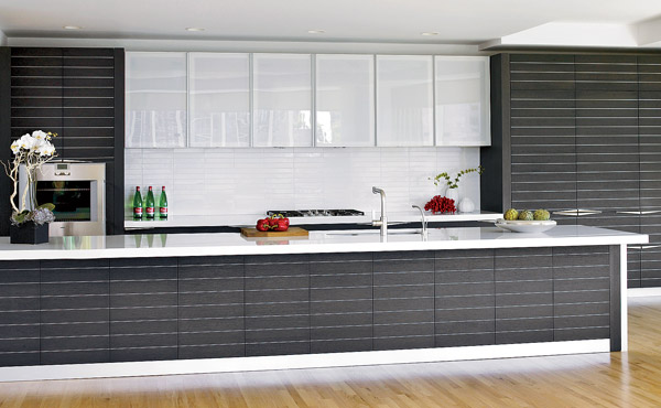 Horizontal lines created by aluminum inlays in the charcoal-stained rift-cut oak cabinetry accentuate the generous length (15 feet) of the island. Its polished white quartz countertop echoes the reflective glass-front cupboards and tile over the cooktop.