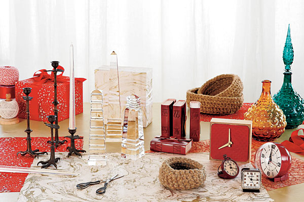 A twine stand, an elegant pair of scissors with black horn handles, blackened brass clawfoot candlesticks, clean-burning, virtually dripless palm-oil candles resemble aerated glass; lighted, they glow from within, crystal obelisks, handmade leather-bound journals, crocheted jute baskets, glass decanters, SuperJumboDeluxe clock with birch plywood frame, Newgate red Bubble alarm clock, and Newgate vintage-style small red and black alarm clocks. Throughout, handmade wrapping papers