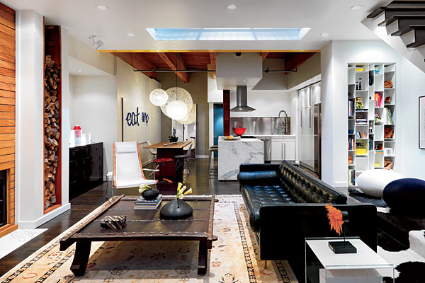 A structural glass inset in the ceiling brings extra light into the living room from the level above. The carpet and the coffee table (made from a vintage ox cart) were purchased at the now-closed Fenway Gallery; oak flooring was stained ebony. In the kitchen, Ikea cabinets are complemented by countertops of statuary marble.