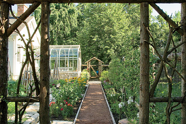 At the end of the path, climbing roses and sweet autumn clematis grow on archways made of rough-hewn logs. Orderly gravel paths and flagstones make plants easy to reach.