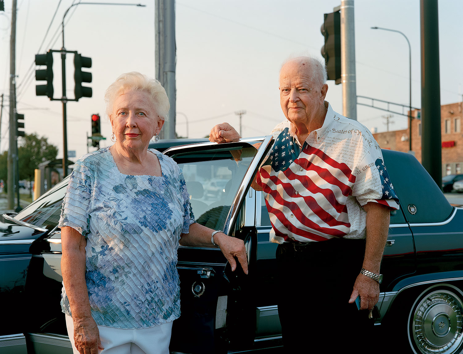 Elderly couple posing in front of their car