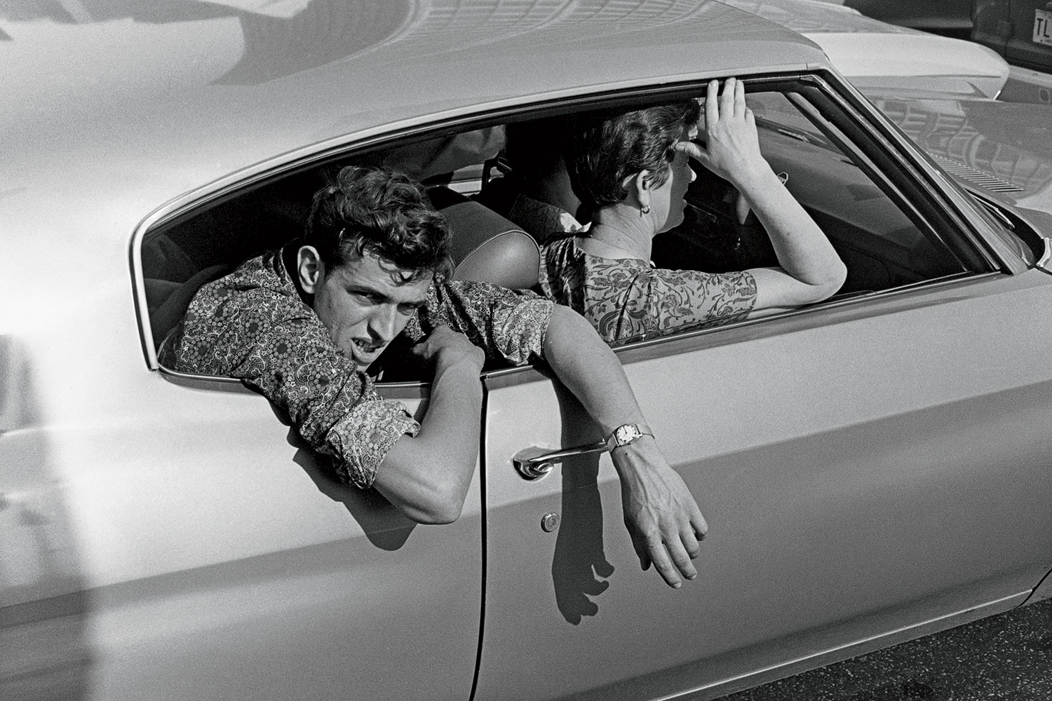 A 1971 photo of a man hanging out of a car to cool off.