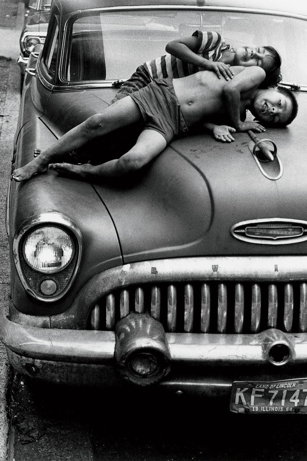 A 1964 photo of two kids lying on the hood of a car in Uptown.
