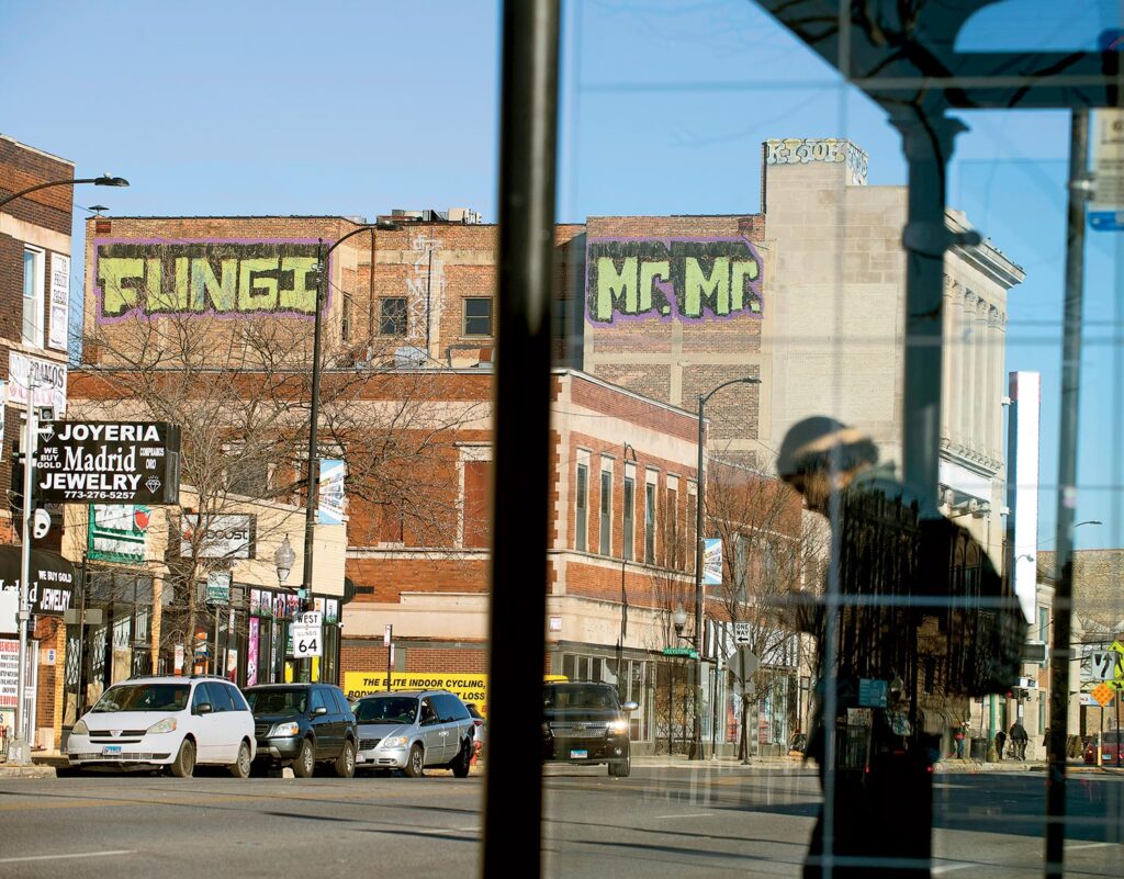 A "Mr. Mr. Fungi" tag just below the roof of a building, as seen near a bus stop.