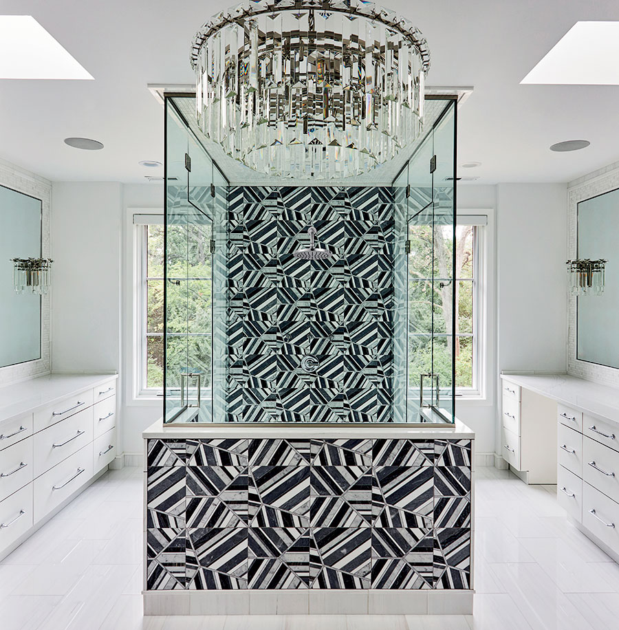 The marble wall of the primary bathroom’s shower plays off a retro chandelier.