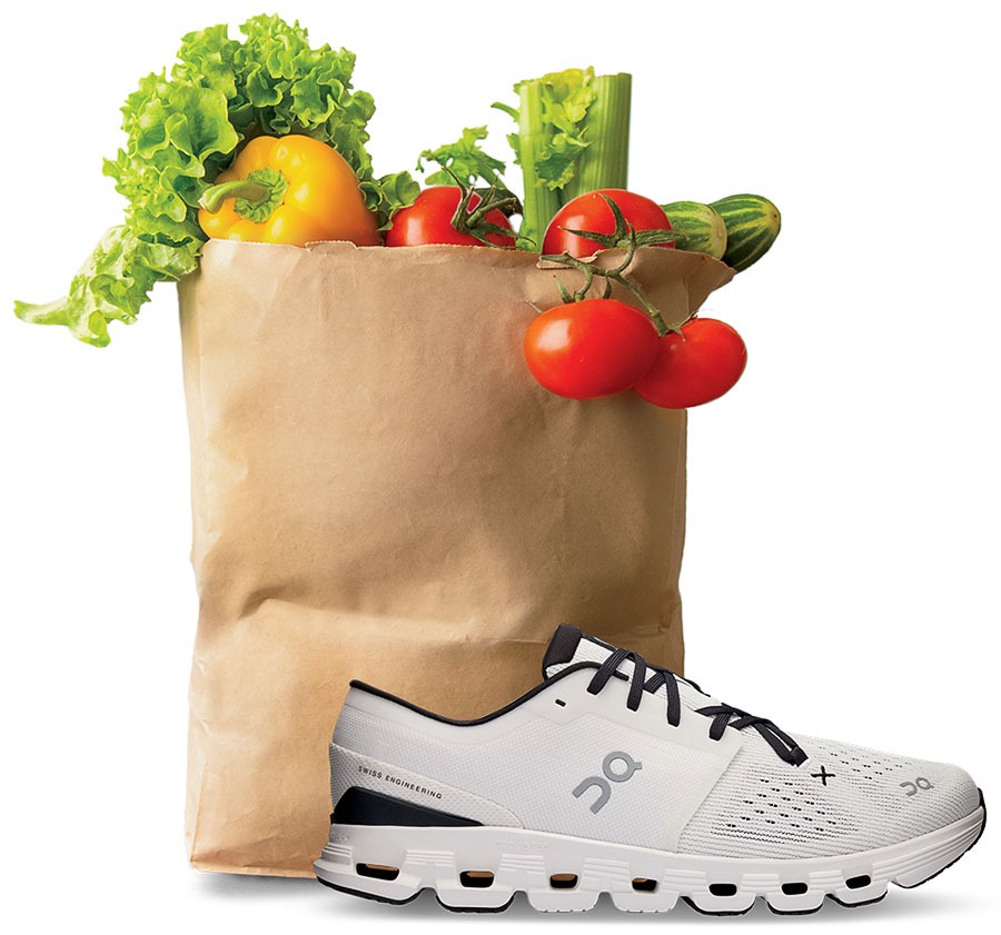 A paper grocery bag full of various vegetables and an On sneaker