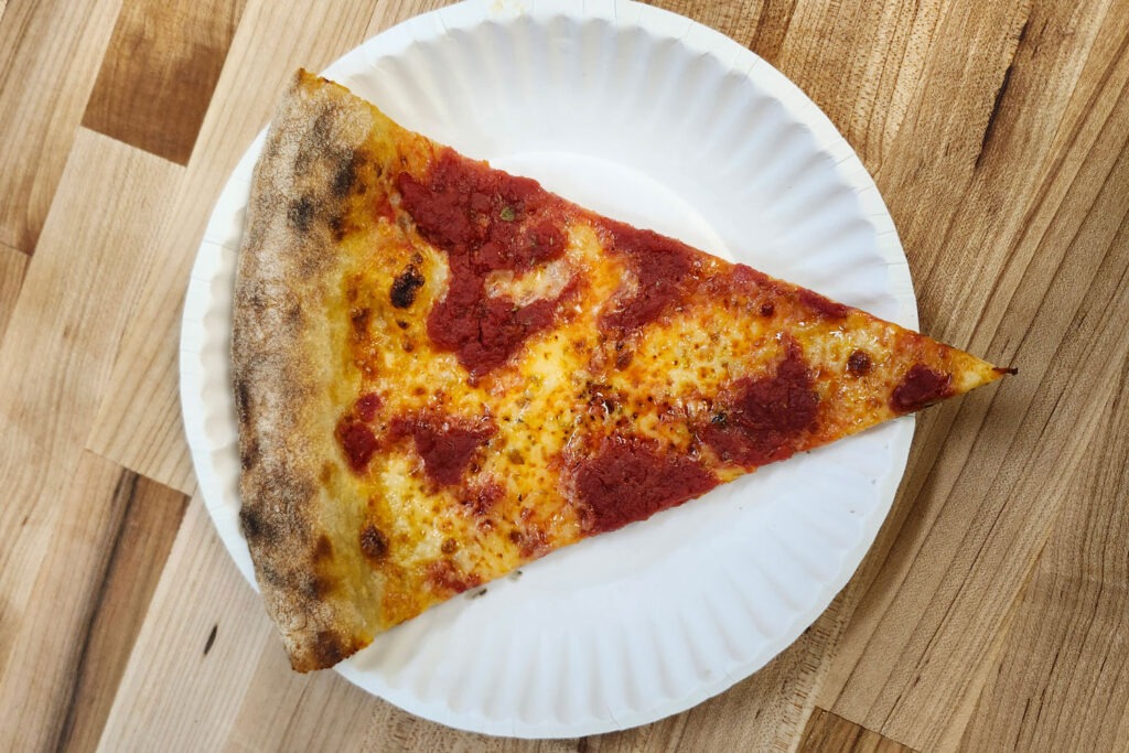 A slice of pizza on a paper plate at Chomp Pizza