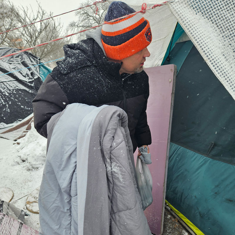 A man in a Bears hat and holding a blanket looks into a tent