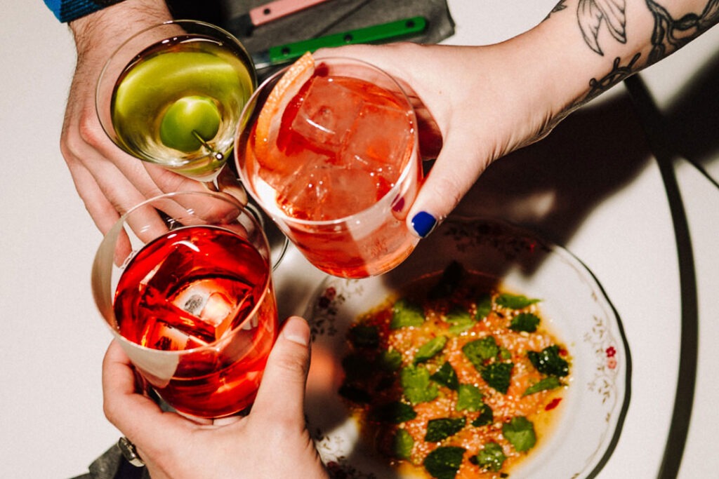 Three hands holding cocktails and toasting at Bar Bambi