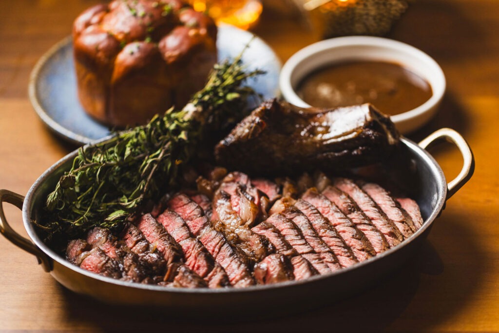 A sliced steak, herbs, sauce, and roll at Susu