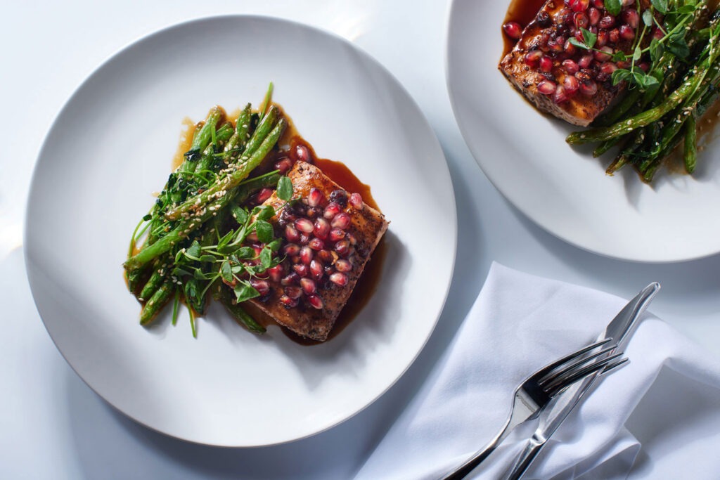 A plate with meat covered in sauce and pomegranate seeds and asparagus at Spice by CMB