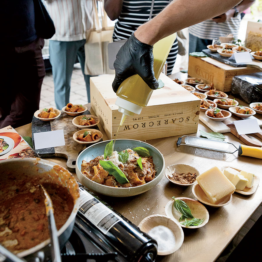 A chef pouring olive oil on a bowl of pasta
