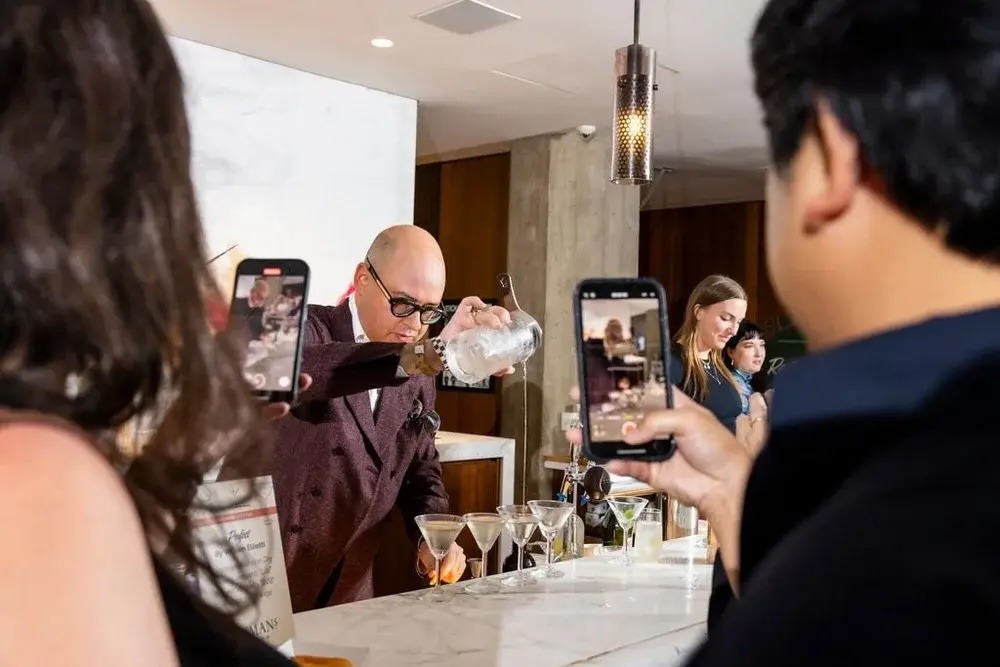 A bartender pouring a martini into a glass as attendees watch.